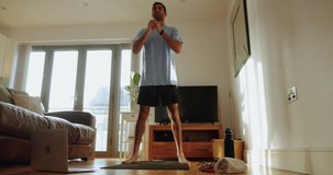 Mixed race male exercising in living room squatting on gym mat feeling good before work