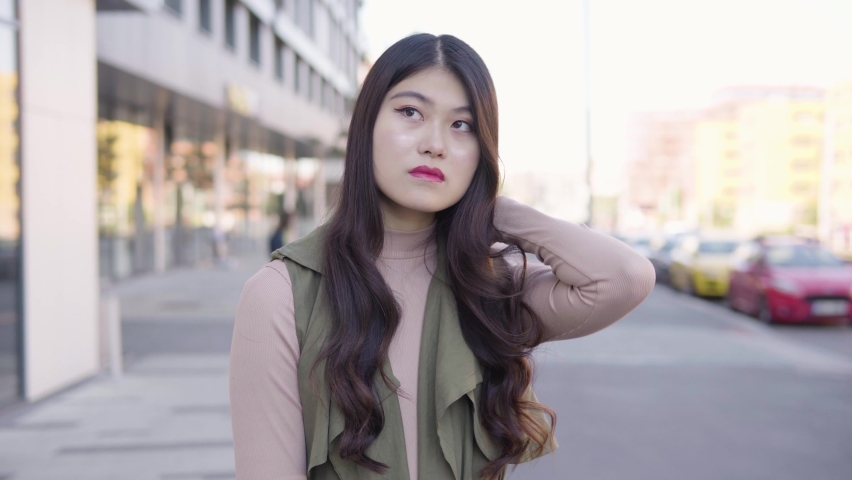 A young Asian woman thinks about something as she waits in a street in an urban area | Shutterstock HD Video #1070281531