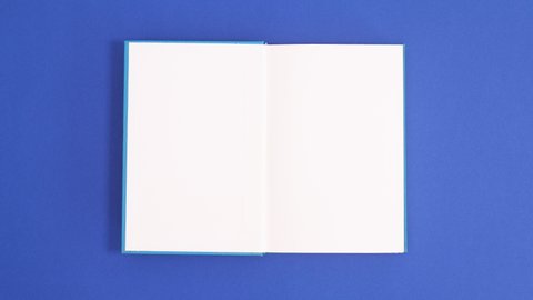 6k Blue vintage hardcover book appear and open with copy space on blue background. Stop motion flat lay