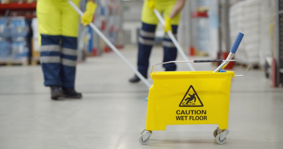 Cropped shot of worker swearing safety overall holding mop cleaning floor in warehouse. Team of janitors with bucket washing floor in industrial storehouse | Shutterstock HD Video #1070283802