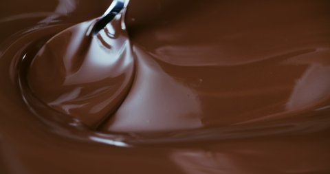 Close-up stirring chocolate with metal pastry spoon, hot melted liquid chocolate, mixing molten milk chocolate or dark caramel. Cooking handmade chocolate dessert and candies. Confectionery