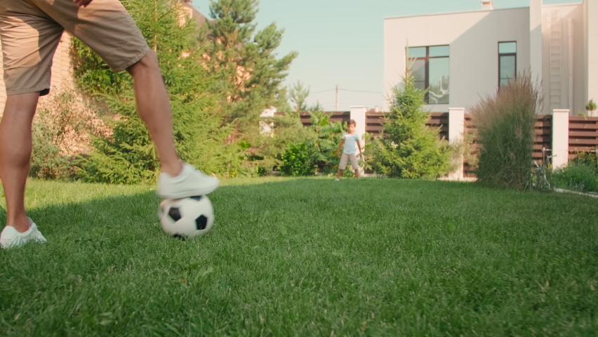 Handheld low-angle shot of modern young adult man playing football with cute 8-year-old son on sunny summer day in backyard having fun together Royalty-Free Stock Footage #1070287588