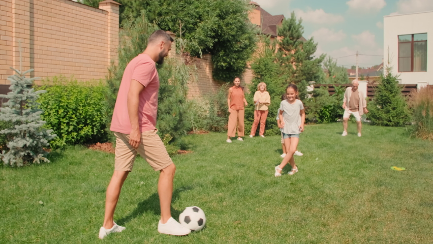 Slow-motion full shot of young adult man dribbling on lawn while big multigeneration family playing football in backyard on sunny summer day Royalty-Free Stock Footage #1070292913