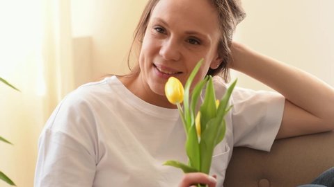 Attractive caucasian woman smiles and enjoys the scents of yellow tulips in the home interior.Mother's day, 8 March and Birthday concept.Close up, slow motion.
