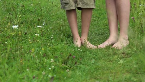 Closeup view video footage of mother and son walking together barefoot in countryside summer landscape. Female legs and young boys legs walking towards camera isolated on grassy ground background