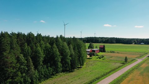 Aerial view overlooking a farm and green field, wind power turbines background, summer in North Europe - rising, drone shot