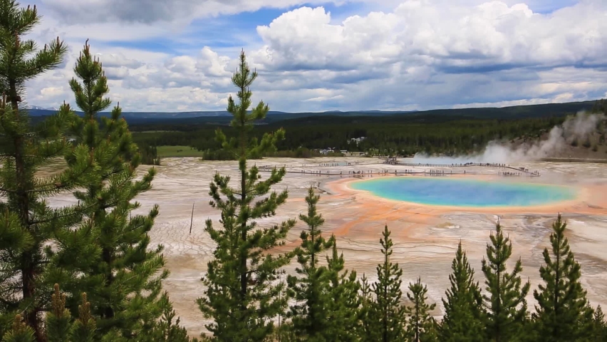 Stunning panning view across turquoise geothermal geyser Grand Prismatic Spring with steam cloud rising and mountains in the background at Yellowstone National Park, Wyoming, USA.