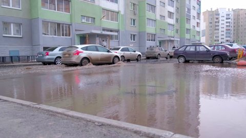 04.04.2021, Russia, Chelyabinsk: White car drives through a huge puddle. Problems of public utilities and roads. 
