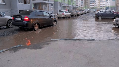 04.04.2021, Russia, Chelyabinsk: black and purple cars drives through a huge puddle. Problems of public utilities and roads. 