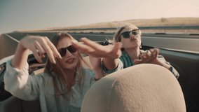 Two young women in sunglasses sing and dance with their hands sitting in back seat of convertible. Girls sing and enjoy ride car without roof in back seat, rear view of track - Powered by Shutterstock - Get 15% off with code: PIKWIZARD15