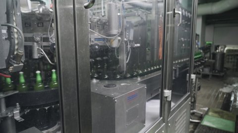 Technological line for beer bottling at the brewery. Technological process of bottling beer in green bottles at the brewery. Brewing concept. Automatic filling machine pouring beer in a brewery.