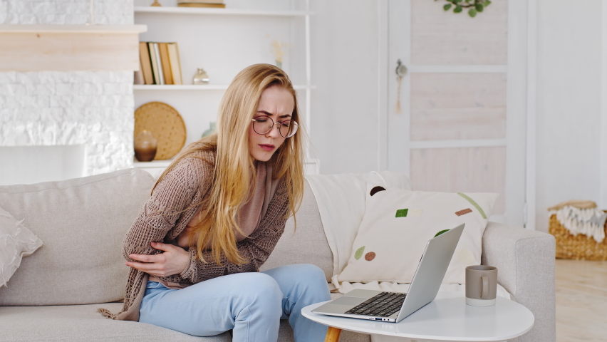 Young blonde girl student wearing glasses caucasian millennial woman working studying at laptop at home online feeling abdomen pain suffering from spasm stomach ache belly abdominal diarrhea disease