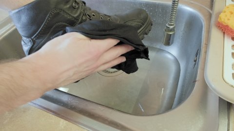 Man washes his shoes for the cold season in an iron sink. He gently wipes his leather shoes with a soft cloth. The concept of careful shoe care