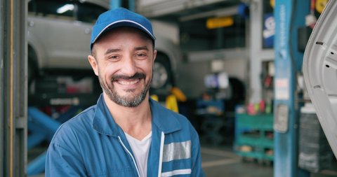 Smiling car mechanic standing look at camera in garage, Portrait of Caucasian man technician master in uniform in front of automobile. Repairing car service concept