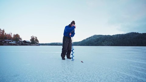 Man Drilling On Ice Using Auger Drill - Ice Fishing At Frozen Lake In Winter At Norway. - wide shot