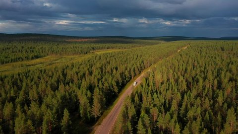 Aerial drone view following a Camper van on a arctic forest road, driving towards dark, stormy clouds