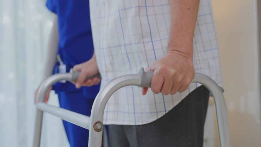 Close up a hands of Asian young woman nurse at nursing home taking care disabled elderly man. Caregiver doctor giving a physical therapy for older patient practice walking on walker or cane at house. | Shutterstock HD Video #1070335636