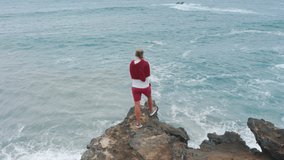 Overhead view of man standing on cliff at atlantic ocean at Capelinhos Volcano, Faial Island, Azores, Portugal, Europe. Drone shot male traveler looking ocean waves, 4k footage