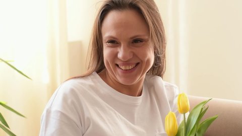 Attractive caucasian woman smiles and enjoys the scents of yellow tulips in the home interior.Mother's day, 8 March and Birthday concept.Close up, slow motion.
