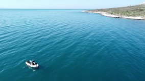 An aerial drone video of a fisherman boat floating in the Ionian sea bay close to the shoreline of Sarande, Albania on a sunny winter's day.