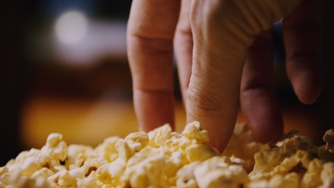 Close up of a man holding a popcorn while watching a movie in the living room.