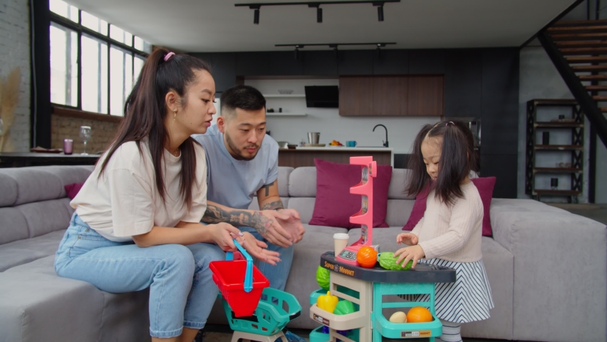 Cheerful attractive asian parents playing with adorable baby daughter in cognitive game, imitating shopping in supermarket during play, expressing carefree mood, care and happiness at home. Royalty-Free Stock Footage #1070348014