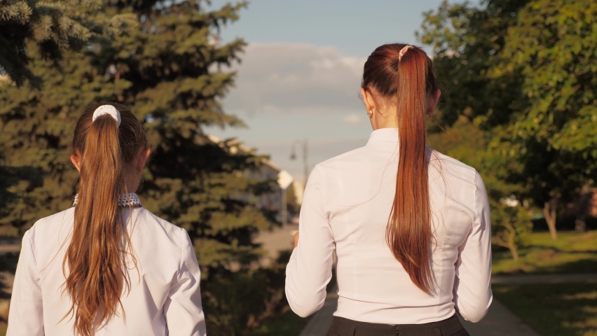 School Girls walk down street in spring, holding textbooks and a tablet. School education concept. Modern methods of study with tablet and traditional with book. Teenagers go to school in park.