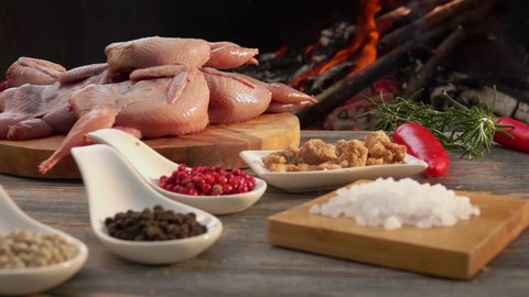 Close-up panorama of the ingredients for preparations of tasty grilled quails on the background of an open fire. Sea salt and peppers next to the raw quails