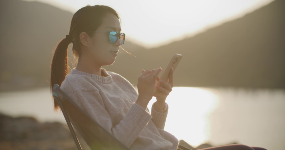 Woman use of mobile phone under sunset