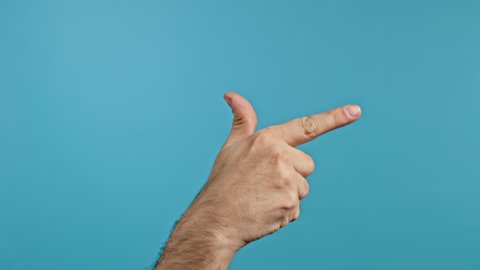 Hand of man doing shot, showing fire gun or weapon, gesture with finger isolated on blue studio background.