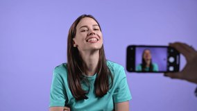 Smiling fashion blogger woman making online new video blog, vlog, with her smartphone on purple background. Influencer speaking to camera during conference call record.