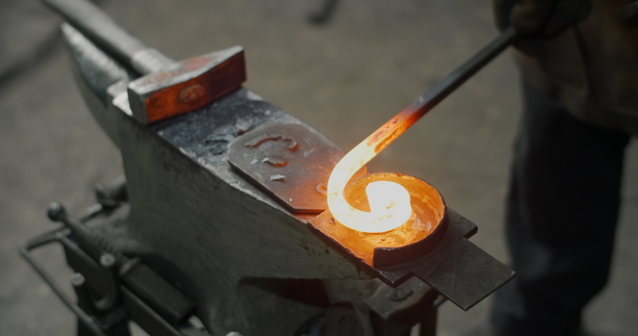 Blacksmith bends a red-hot metal rod on an anvil into a spiral, decorative blacksmith craft, forged metal, 4k 60p Prores HQ Royalty-Free Stock Footage #1070359738
