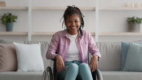 Happy Disabled Black Teen Girl Posing In Wheelchair Smiling Looking At Camera At Home. Positive Impaired Paralyzed Female Teenager Sitting In Wheel Chair Indoor. Life With Disability. Zoom In Shot