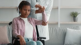 Doctor Physiatrist Massaging Paralyzed Arm Of Handicapped African Girl In Wheelchair Indoors. Physiotherapy For Disabled Child, Recovery And Rehabilitation After Injury Concept. Cropped