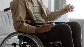 Unrecognizable Disabled Black Man In Wheelchair Drinking Whiskey Holding Glass Of Booze At Home. Handicapped Guy Suffering From Disability Depression And Alcohol Addiction Problem. Cropped