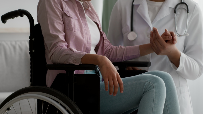 Doctor Supporting Unrecognizable Handicapped Black Girl Sitting In Wheelchair, Stroking Her Arm During Appointment Indoor. Cropped, Closeup. Physical Therapy And Rehabilitation After Injury | Shutterstock HD Video #1070361922