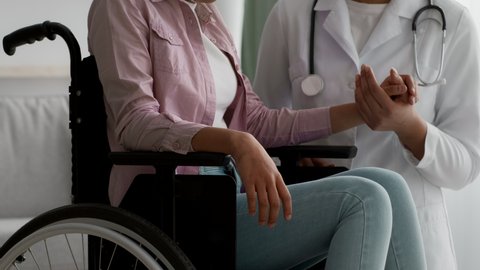 Doctor Supporting Unrecognizable Handicapped Black Girl Sitting In Wheelchair, Stroking Her Arm During Appointment Indoor. Cropped, Closeup. Physical Therapy And Rehabilitation After Injury