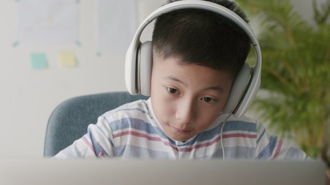 Asian little boy video call online via the internet tutor on a computer laptop with headphones. Asia man doing homework. Concept online learning at home
