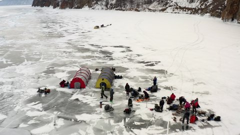 Aerial view. Drone flight over tourists camping with a tent and getting ready to sleep on the ice. A tent on the frozen Lake Baikal and tourists are preparing for the night.