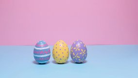 Video of Happy Easter. Colorful painted Easter eggs roll and knock each other on a pink background. Hello spring and easter concept. 4k video.