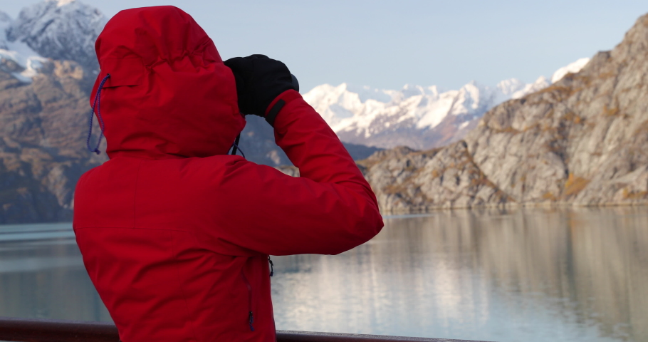 Alaska Glacier Bay cruise ship passenger looking at Alaskan mountains with binoculars exploring Glacier Bay National Park in USA. Woman on travel in Inside Passage enjoying view on vacation adventure. Royalty-Free Stock Footage #1070374930