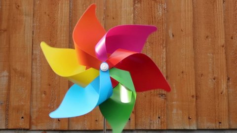 Large single pinwheel or windmill spinning slowly and intermittently or occasionally in the breeze. Rainbow colours. Close up outdoors on a sunlit day in a domestic back garden.