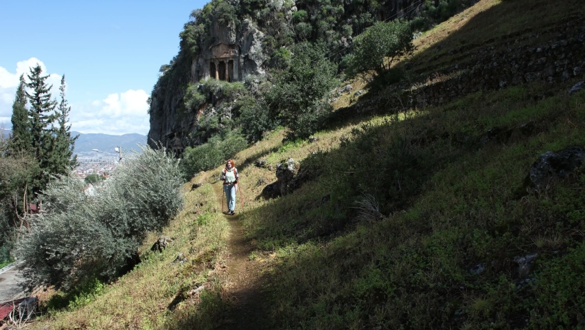 Famous places of resort town of Fethiye in Turkey, Lycian tombs, young woman walks along slope of mountain while walking near monument.