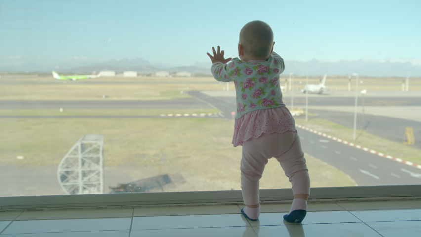Little baby girl looks out of window at airport. Child looking at the plane through the window at waiting hall.