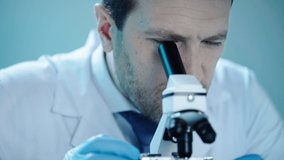 handsome scientist talking while looking in microscope in laboratory