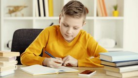cheerful kid holding pen, taking smartphone, smiling and writing in notebook