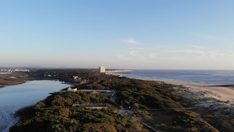 DRONE AERIAL FOOTAGE: The Northern Litoral Natural Park in Ofir, Esposende, Portugal. Wooden boardwalk and the Ofir Towers in the background. Sea, beach boulders, pebble shore and waves at sunset.