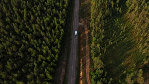 Aerial view following a RV driving on a forest road, in the Nordic wilderness - tilt up, drone shot