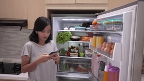 asian young woman using her smartphone to buy groceries while open her fridge at home - Powered by Shutterstock - Get 15% off with code: PIKWIZARD15