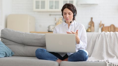 Nervous freelancer mother sitting on couch at home office during lockdown, working on laptop. Little child distracts from work, taking off headphones, making noise and asking attention from busy mom
